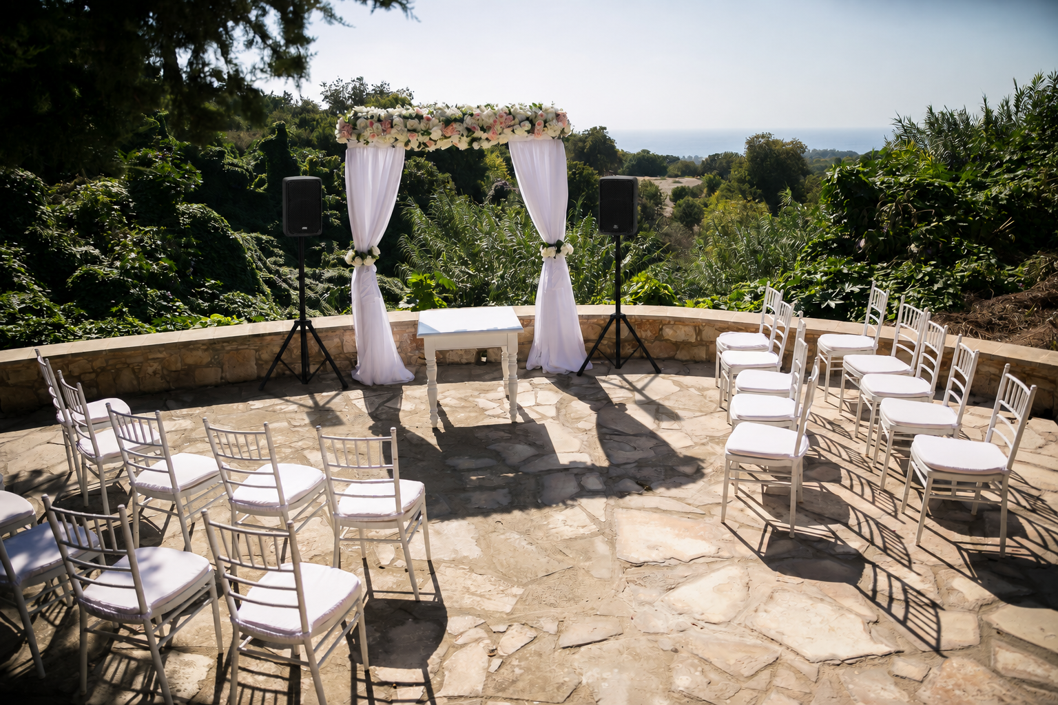 Seaside wedding ceremony with two PA speakers on tripods either side of the floral arch